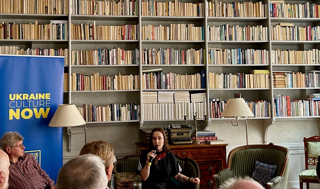 Author Alina Sanatska sitting in front of a wall of books at the Swedish Writer's Union offices in Stockholm